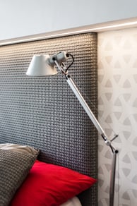 Lampa u postele s čelem a polštáři v interiéru ložnice.